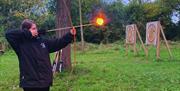 Jess, a young White Dragon Activity Centre coach, shooting a flaming arrow from a longbow in a grassy archery range in autumn