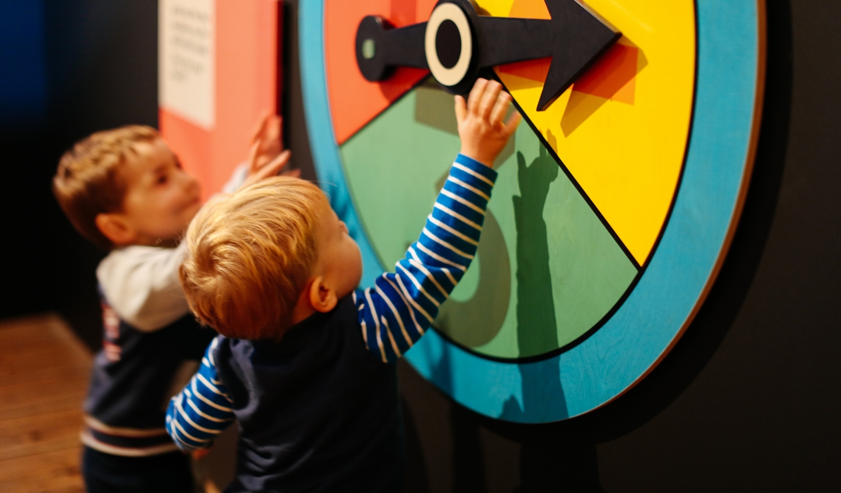 Two children reach up to large brightly coloured  spinner