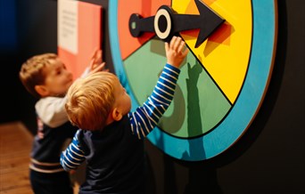 Two children reach up to large brightly coloured  spinner