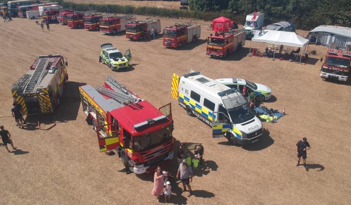Field with a combine harvester, fire engine, tractor, emergency vehicles and a horse