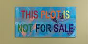 A rectangular sign with the words 'this plot is not for sale' stencilled in bright colours on a blue background with colourful leaf designs.