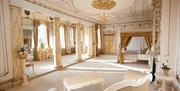 The Rococo Honeymoon Suite. A cream and gold room with a four-poster bed, love seat and dressing table.