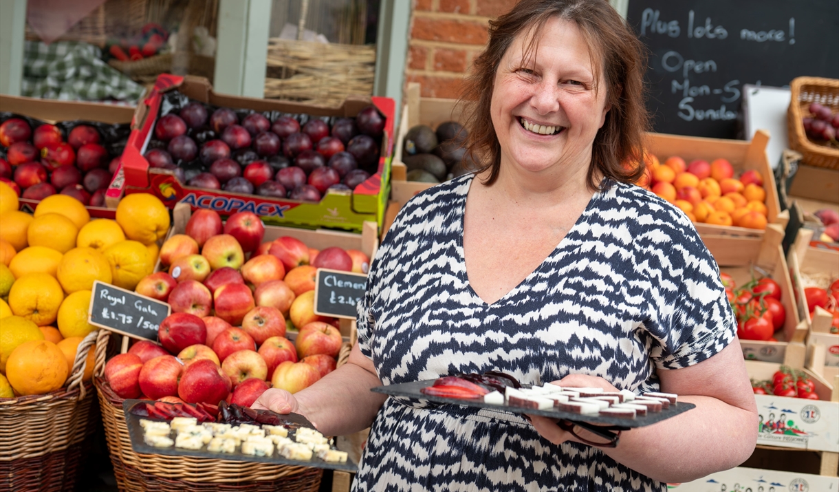 Female holding cheese samples in front of fruit and vegetable display Female holding cheese samples in front of fruit and vegetable display