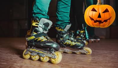 Person with black and yellow roller skates on and a carved pumpkin in the background