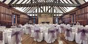 The Great Hall with exposed dark wood beams adorned with fairy lights. Tables set up ready for the wedding breakfast.