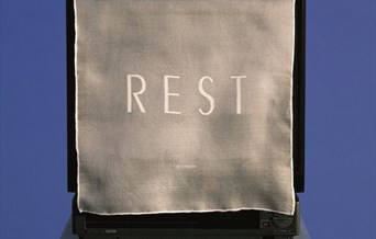 a cloth with the word 'REST' printed onto it covers a monitor or screen