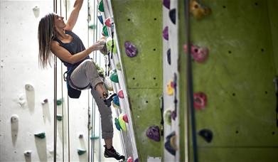 long haired woman climbing up indoor climbing wall