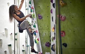 long haired woman climbing up indoor climbing wall