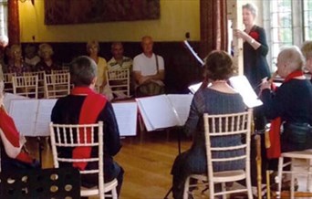 six musicians play to a small audience in a wood panelled hall with a large window