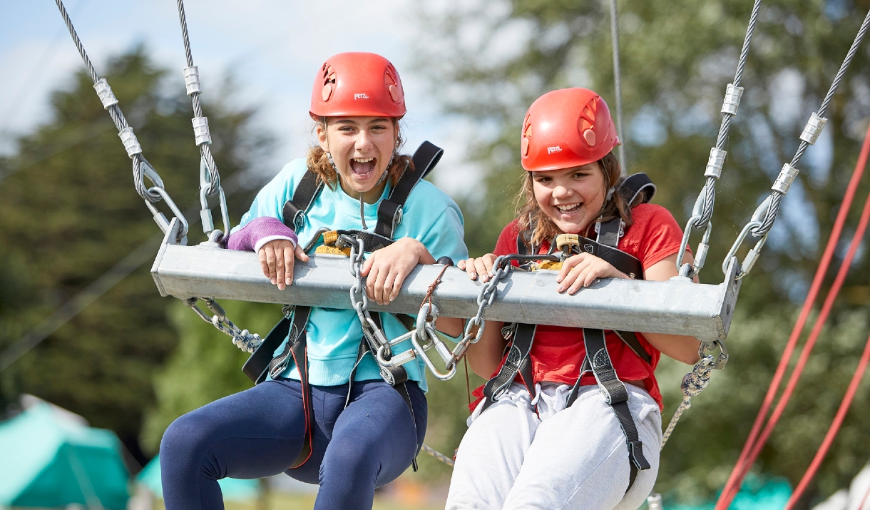two smiling girls wearing red climbing helmets and harnesses
