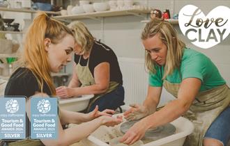 Two ladies throwing a pot at LoveClay Ceramics Centre, infront of them is a studio instructor helping one of the ladies.