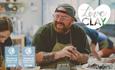 A visitor, with tattooed arms, a ginger beard, glasses and a cap the wrong way around, smiles at his friend