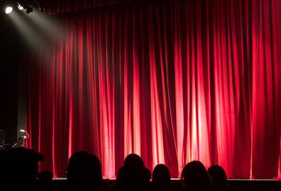 People sitting in a theatre in front of a red curtain