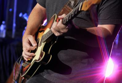 Man in black shirt playing a brown electric guitar