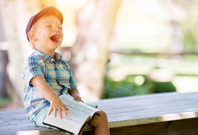 Boy sitting with book on a bench and laughing