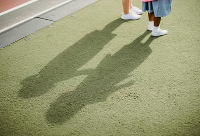 Two children casting shadows on a green surface