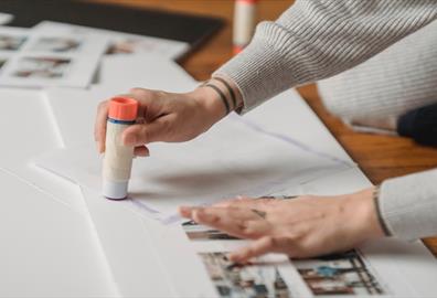 A person with tattoos using a glue stick on paper