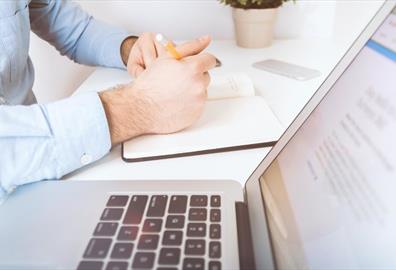 White laptop and man writing in notebook
