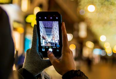 Person with one glove off taking a photo of a Christmas street light display