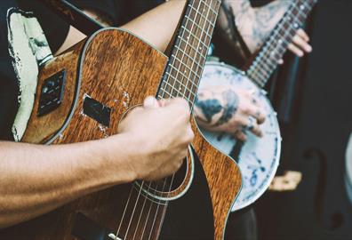 Person playing a banjo and another playing a dark wood acoustic guitar and another with a double bass