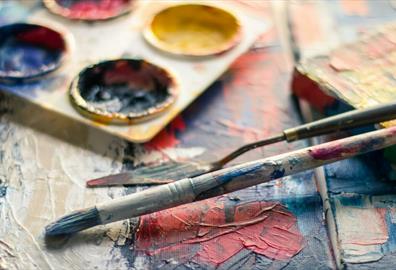 Close-up of colourful paintbrushes and artist palette on a textured canvas