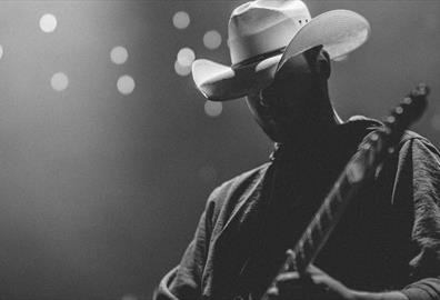 Person wearing a white cowboy hat playing on a lit stage