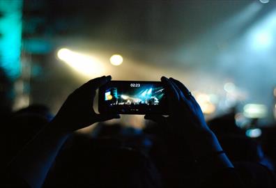 Hands holding a mobile phone taking a picture at a concert