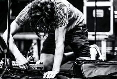 Black and white image of a person plugging in a pedalboard on stage