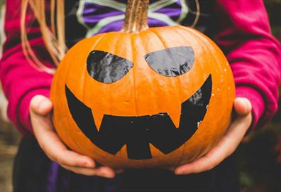 Girl in witch costume holding a smiling pumpkin