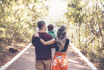 Young family walking in a light forest and carrying their toddler