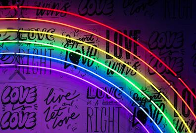 A neon rainbow sign with black writing behind it