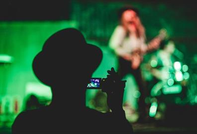 Person recording video of a person playing guitar onstage