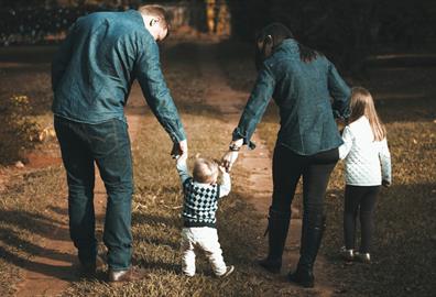 Young family walking a green forest and holding hands with their toddler