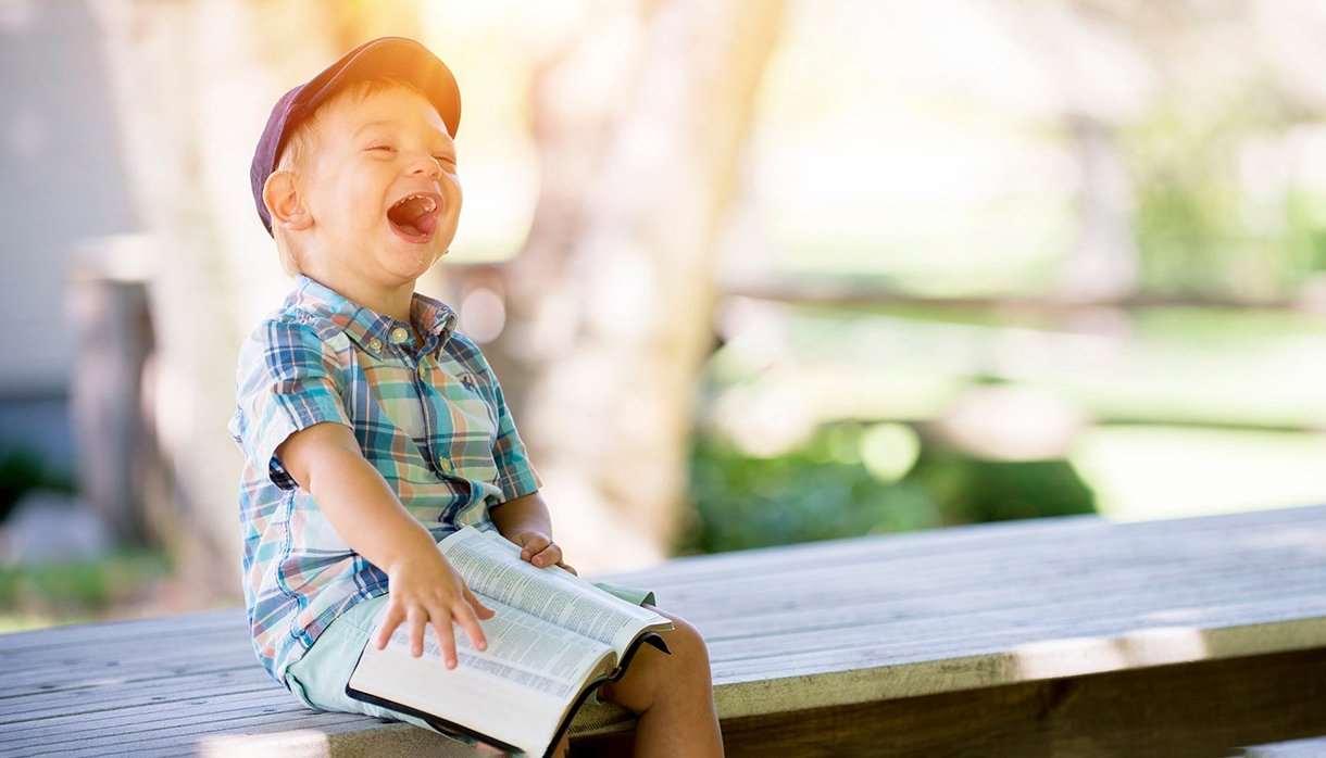 Boy sitting with book on a bench and laughing