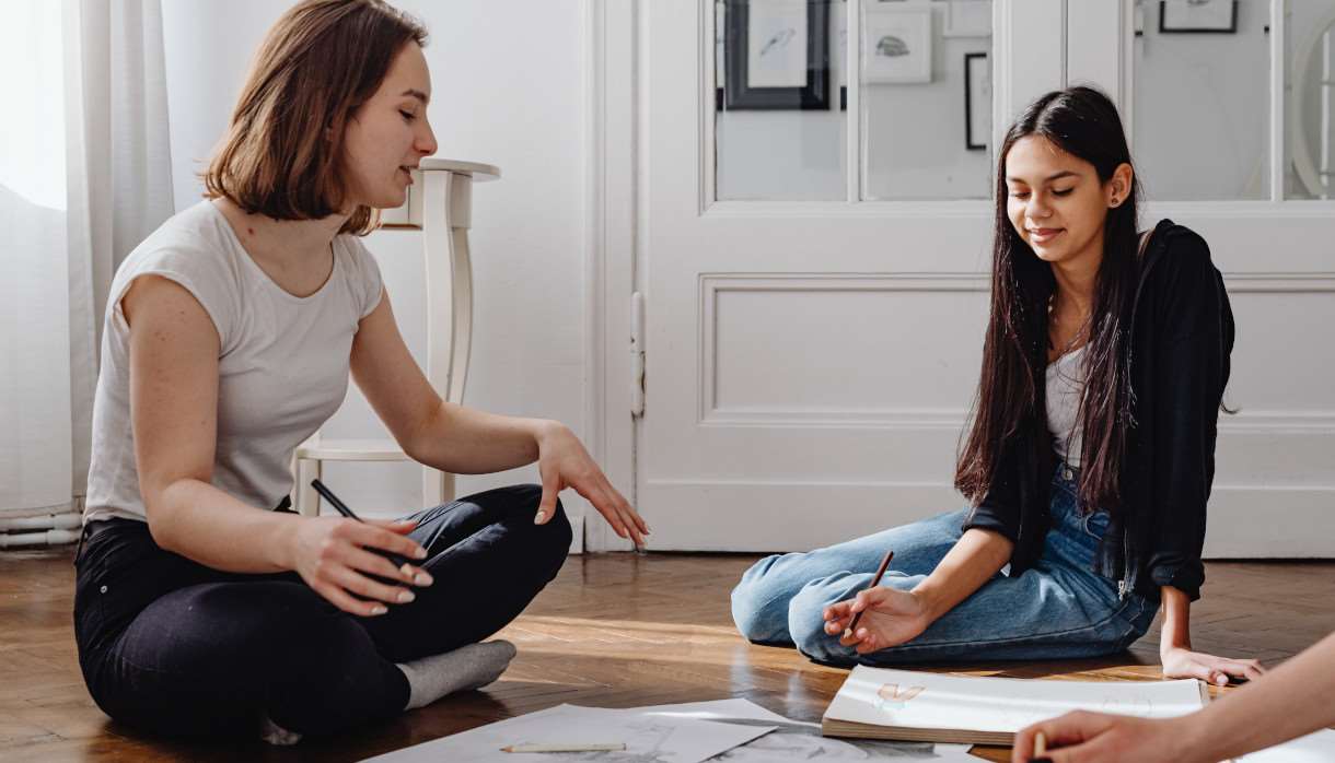 Two people sat on the floor between art supplies