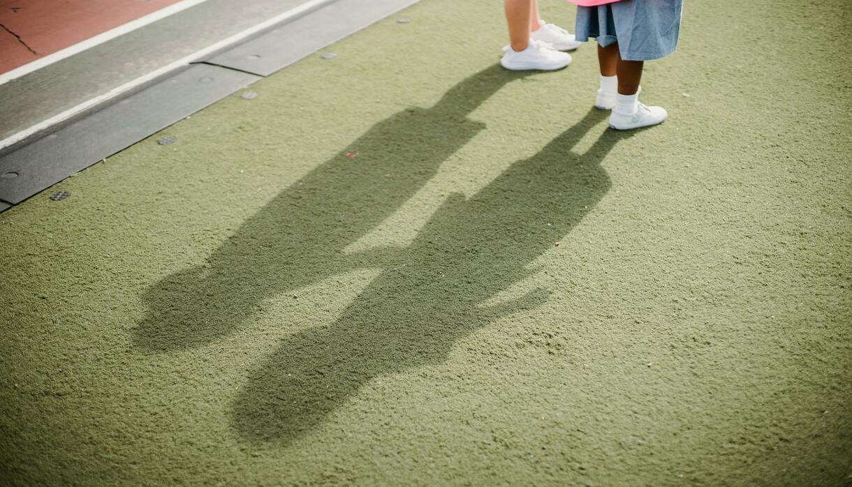 Two children casting shadows on a green surface