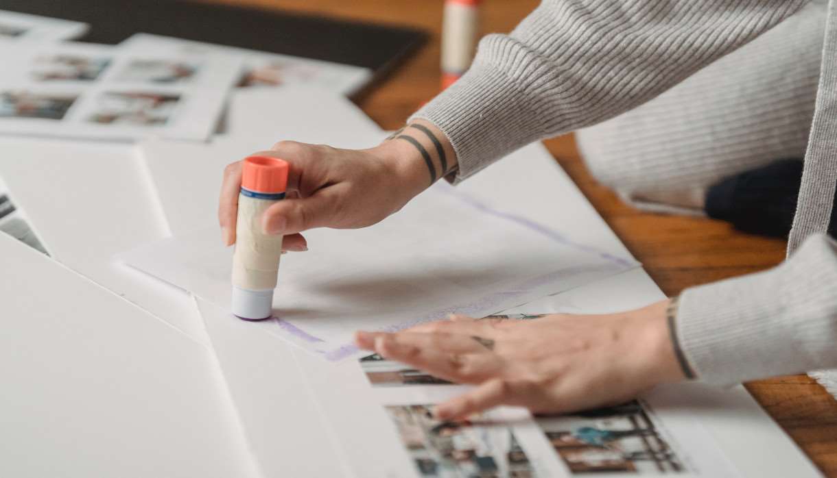 A person with tattoos using a glue stick on paper