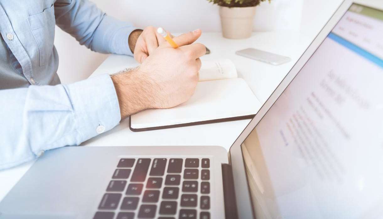 White laptop and man writing in notebook