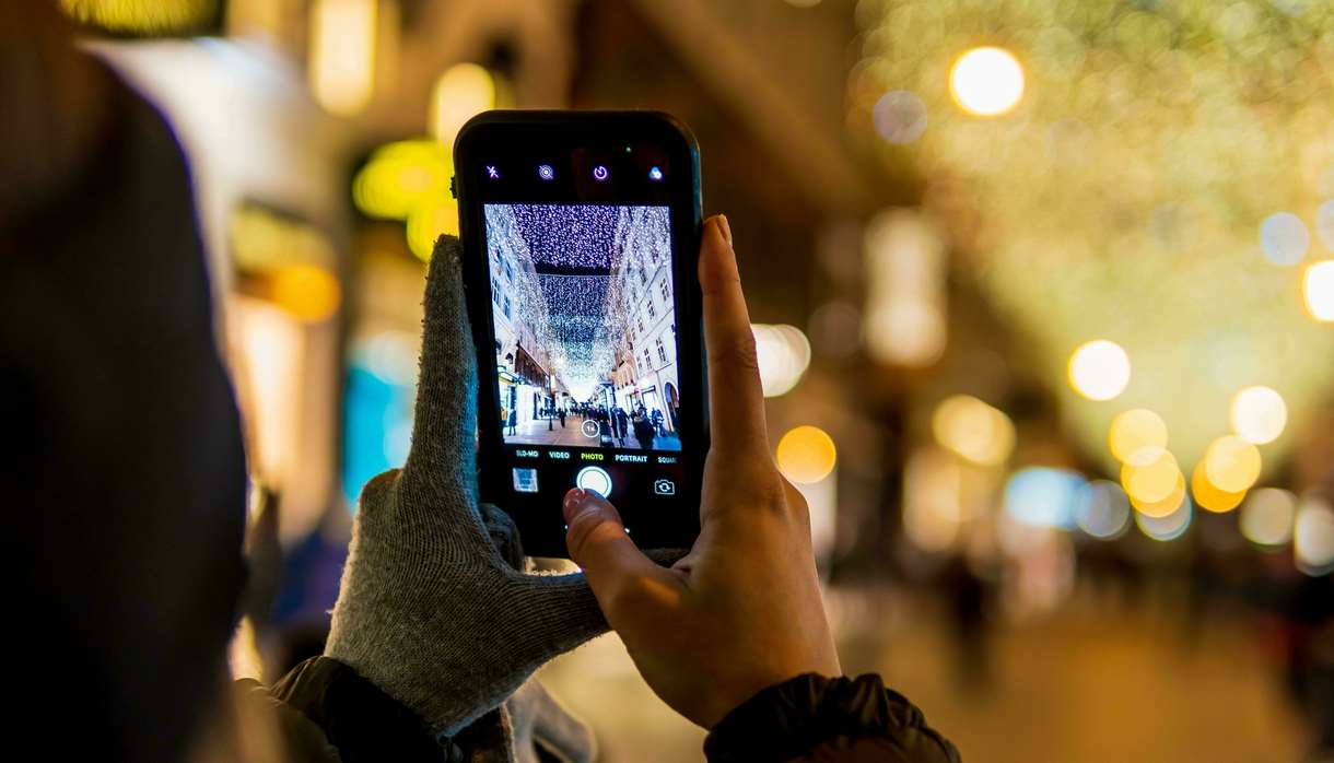 Person with one glove off taking a photo of a Christmas street light display