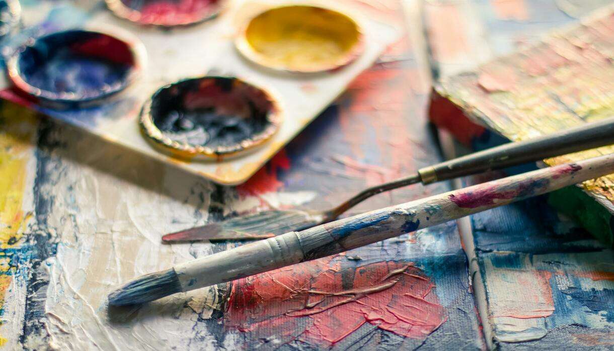 Close-up of colourful paintbrushes and artist palette on a textured canvas