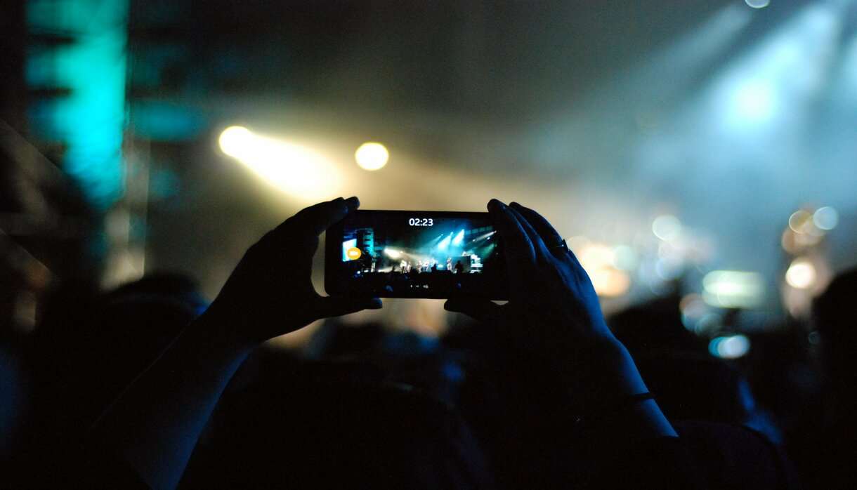 Hands holding a mobile phone taking a picture at a concert