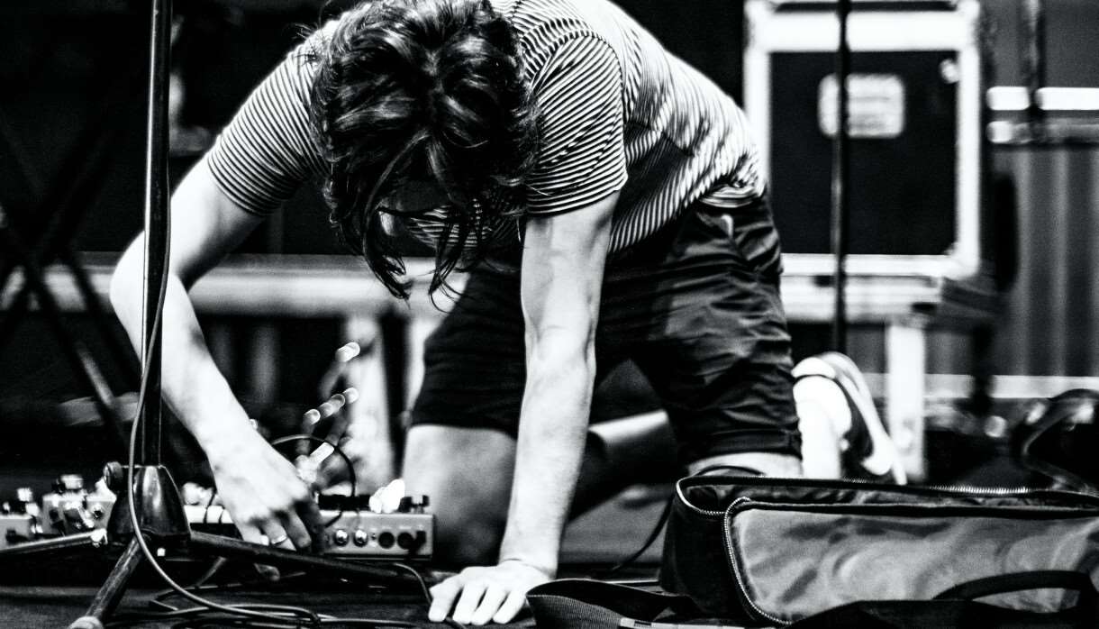 Black and white image of a person plugging in a pedalboard on stage