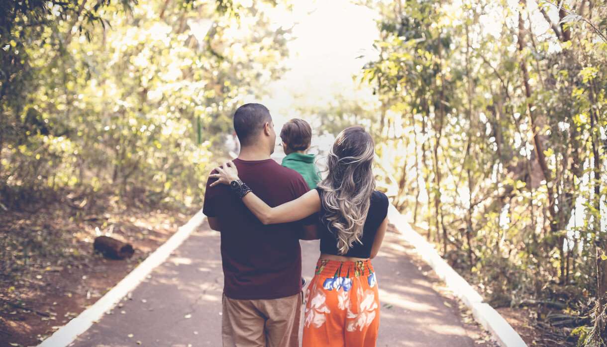 Young family walking in a light forest and carrying their toddler