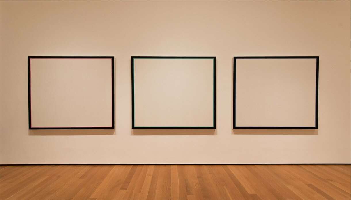 Three blank canvases on a white wall in a gallery with wooden floorboards
