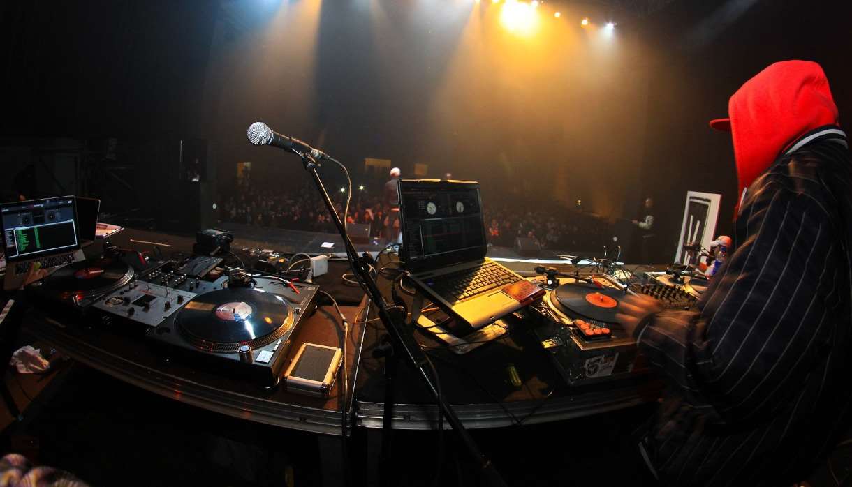 Person in a red hood DJing to a large crowd