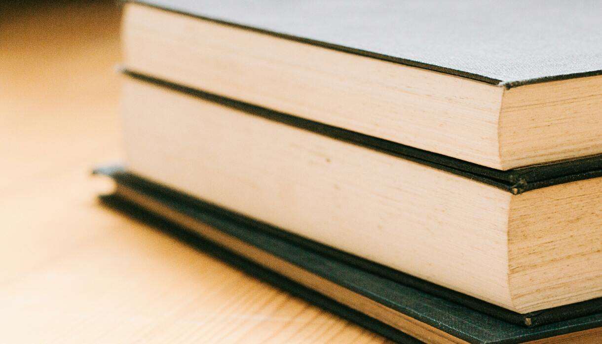 Close-up image of stack of hardcover books on a wooden table