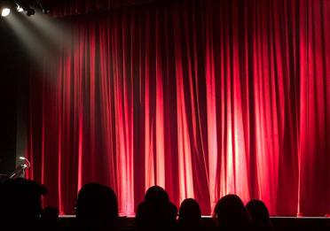 People sitting in a theatre in front of a red curtain