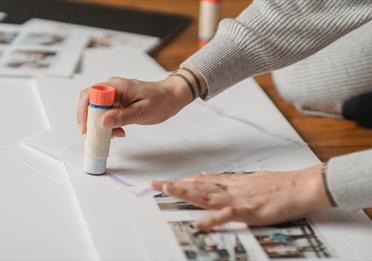 A person with tattoos using a glue stick on paper