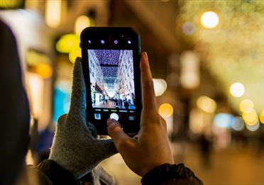 Person with one glove off taking a photo of a Christmas street light display