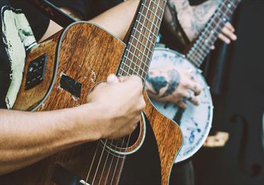 Person playing a banjo and another playing a dark wood acoustic guitar and another with a double bass